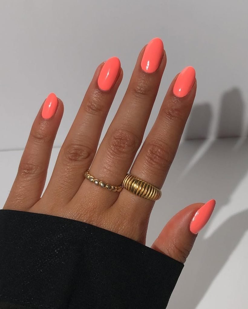 glossy coral pink polish on short oval nails accessorized with gold rings