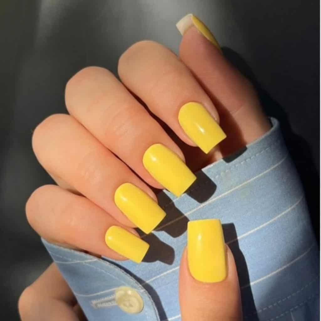 square-shaped bright yellow manicure on a hand wearing a blue striped shirt