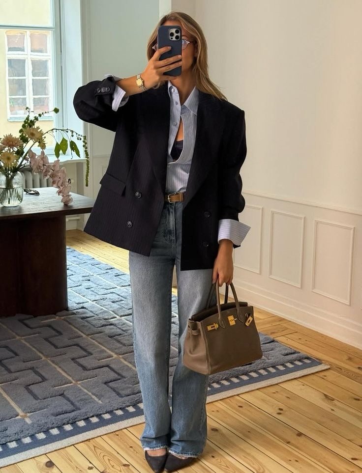 woman wearing oversized black pinstripe blazer, light blue button-down shirt, and wide-leg jeans