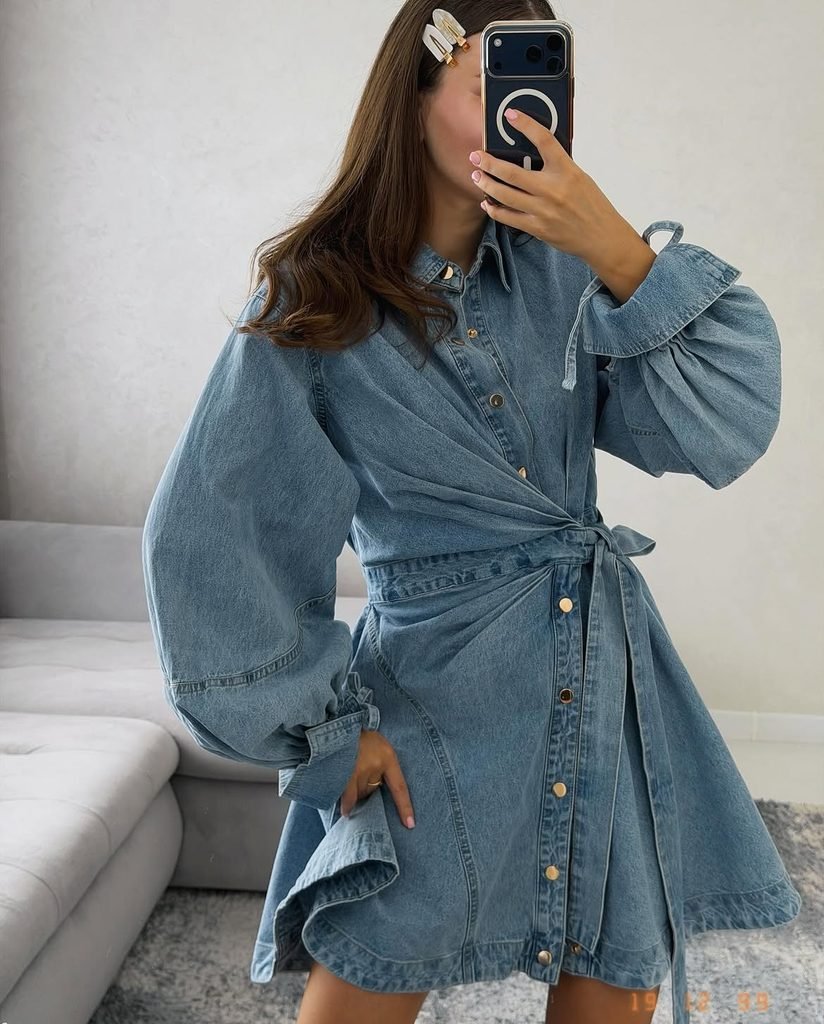 woman wearing long-sleeve light wash denim mini dress with wrap waist and statement sleeves