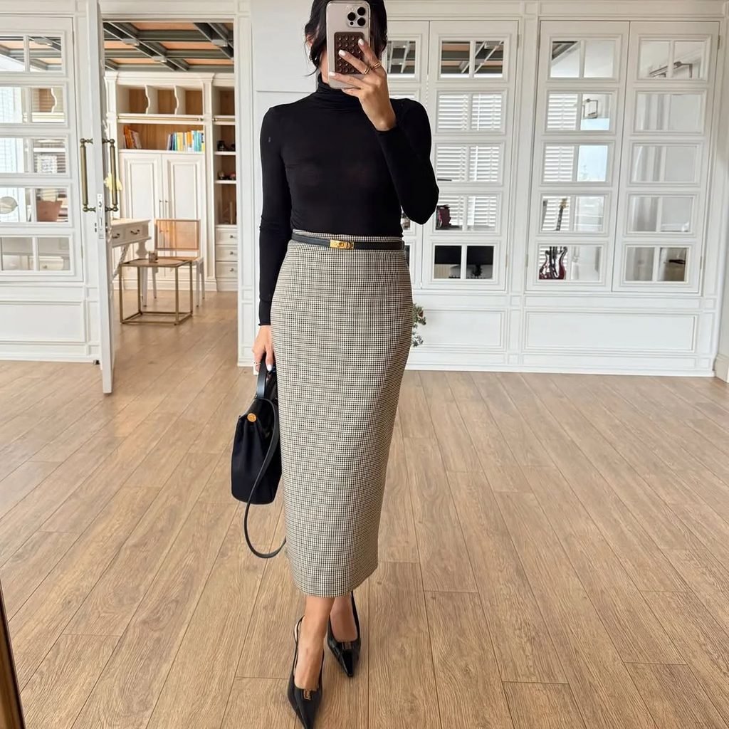 woman in black turtleneck and high-waisted houndstooth midi skirt holding black handbag