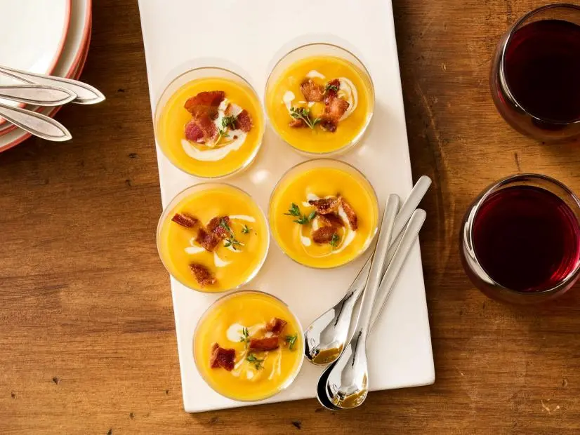 butternut squash soup shooters topped with crispy bacon pieces and fresh herbs on a tray