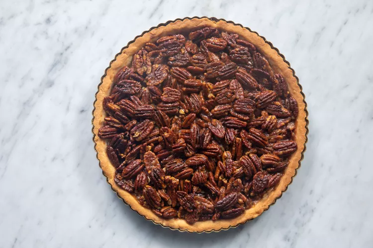 whole caramel pecan tart with fluted crust on a marble countertop