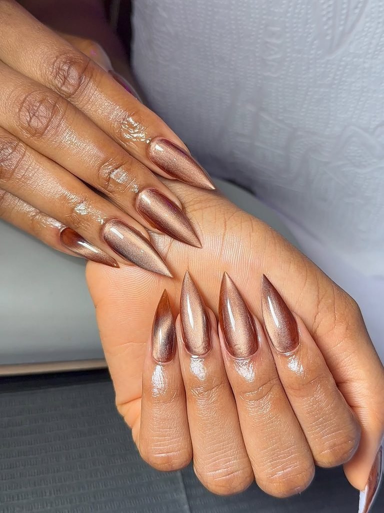 long bronze cat eye nails with sharp stiletto tips on dark skin manicured hands