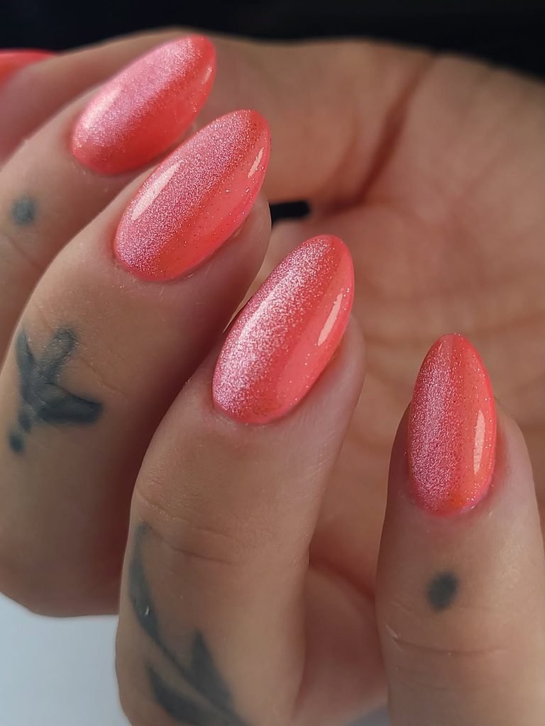 shimmering coral pink cat eye nails on fingers with small tattoos