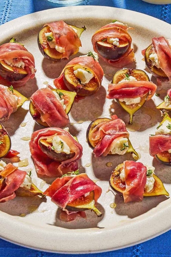 sweet figs stuffed with goat cheese and wrapped in savory prosciutto on a platter