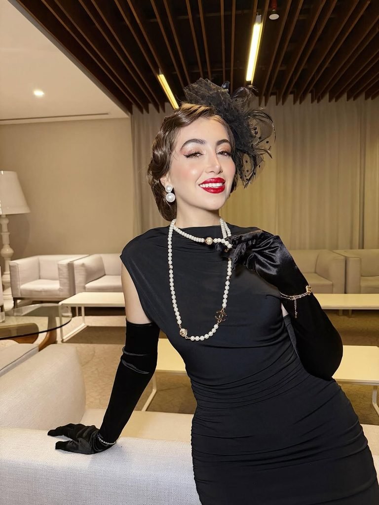 woman wearing a vintage black dress pearl necklace black gloves and fascinator hat