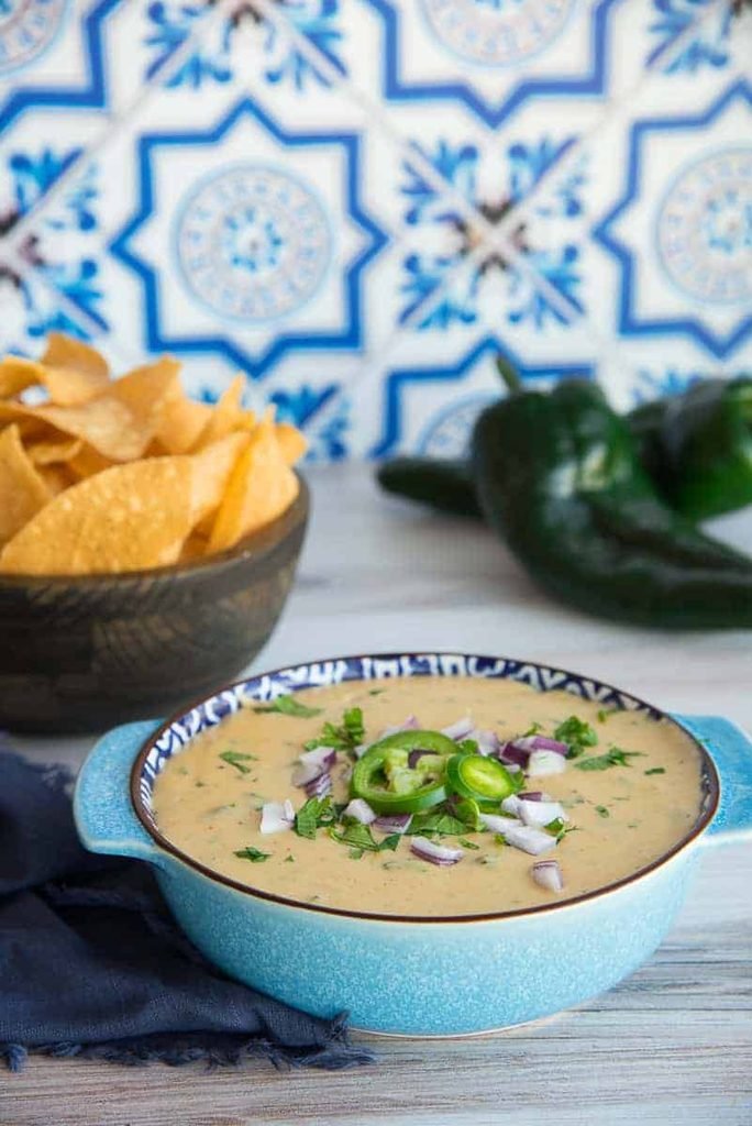 creamy poblano white queso dip topped with diced onions and jalapeños alongside tortilla chips
