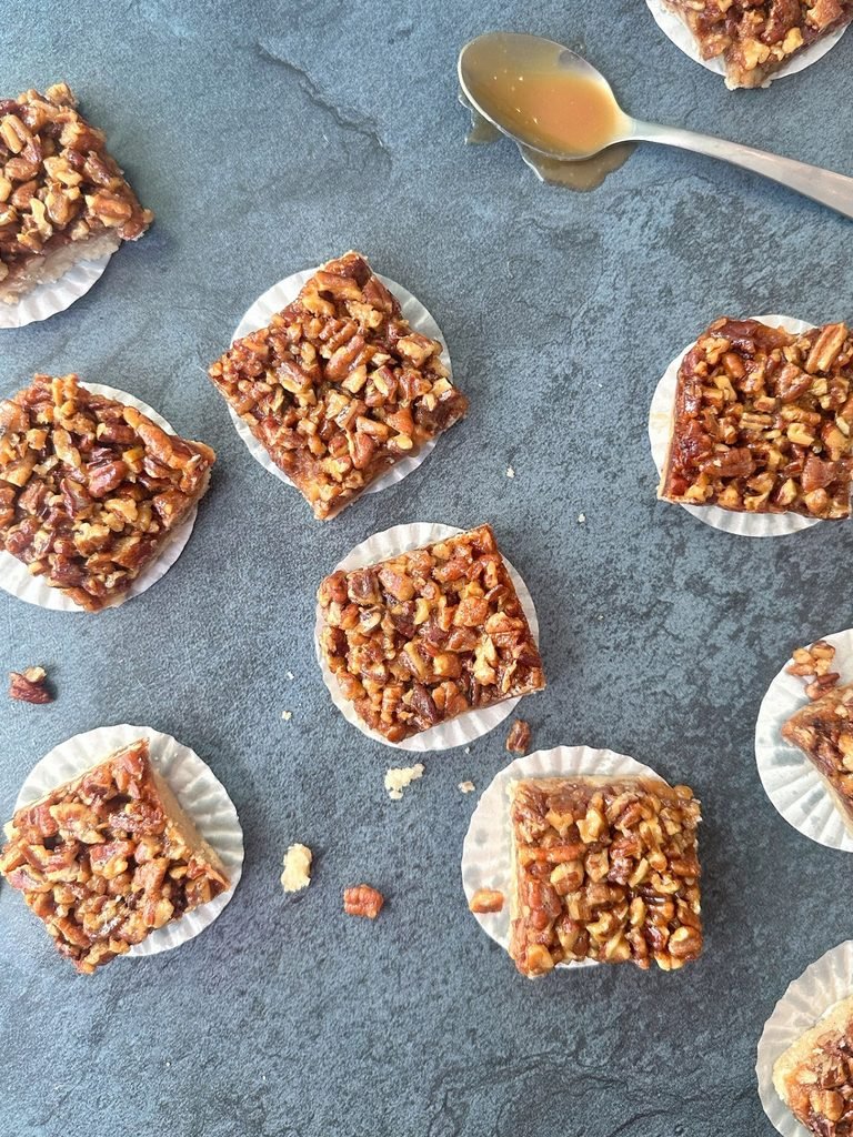 square caramel pecan bars served on individual cupcake liners over slate