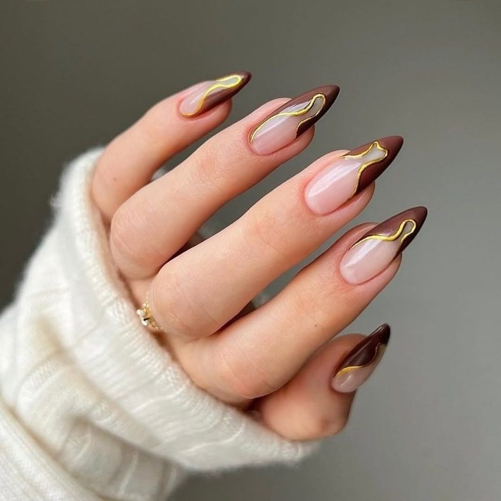 almond nails with nude bases brown french tips and abstract gold swirls