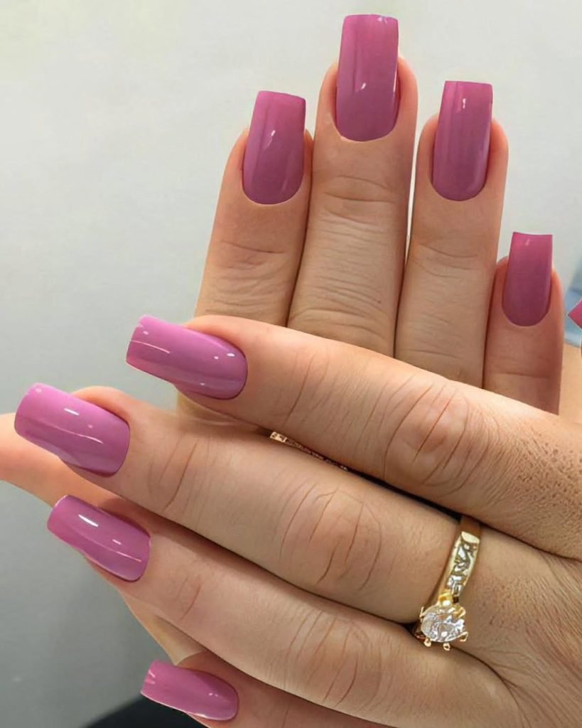 square shaped glossy pink nails on a hand wearing a gold ring