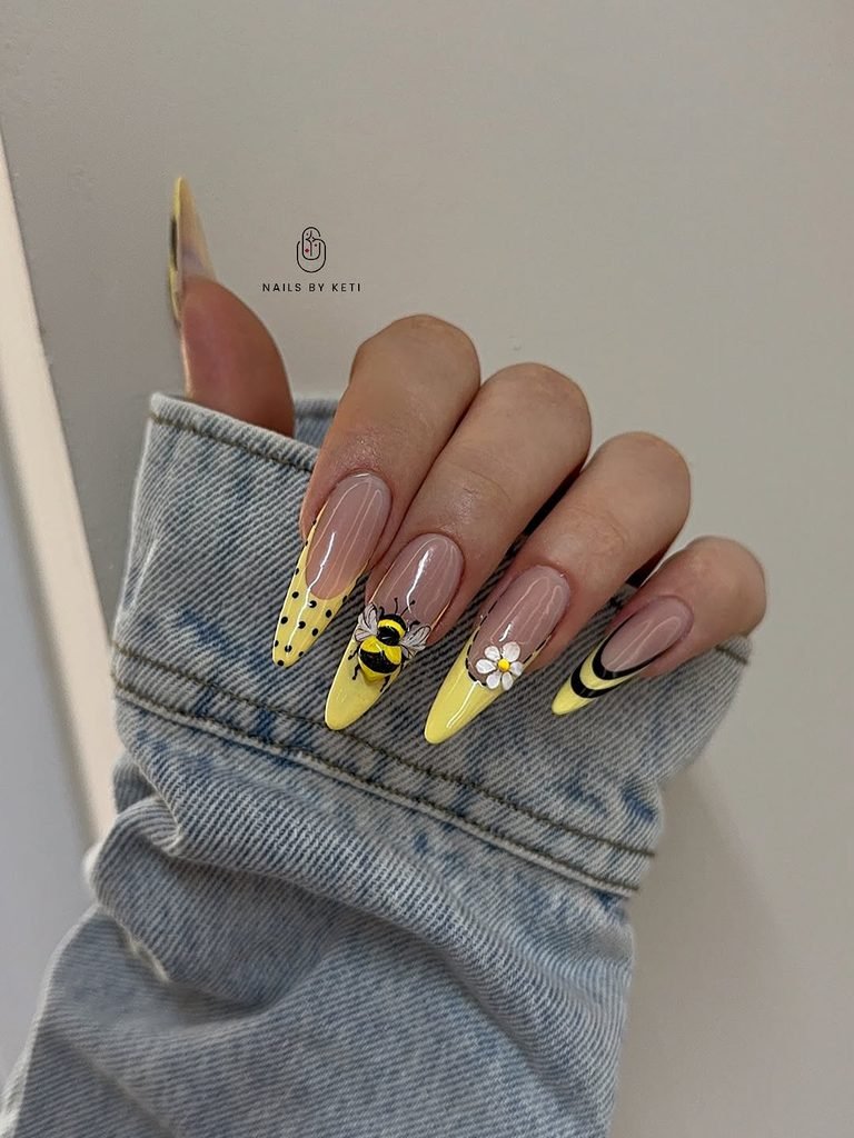 long almond nails with yellow french tips featuring a bee and daisy design