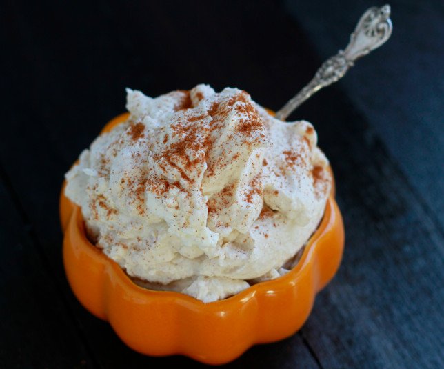 spiced whipped cream dusted with ground cinnamon in a orange pumpkin bowl