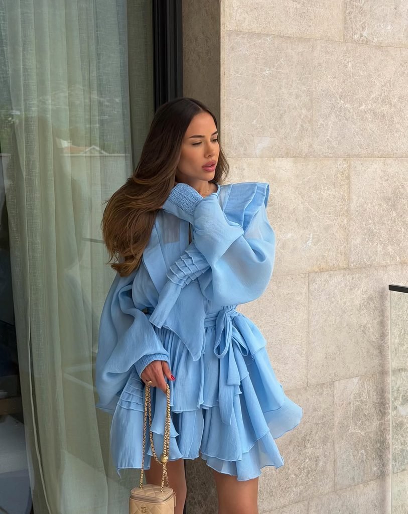 woman wearing a ruffled light blue long sleeve mini dress standing outside