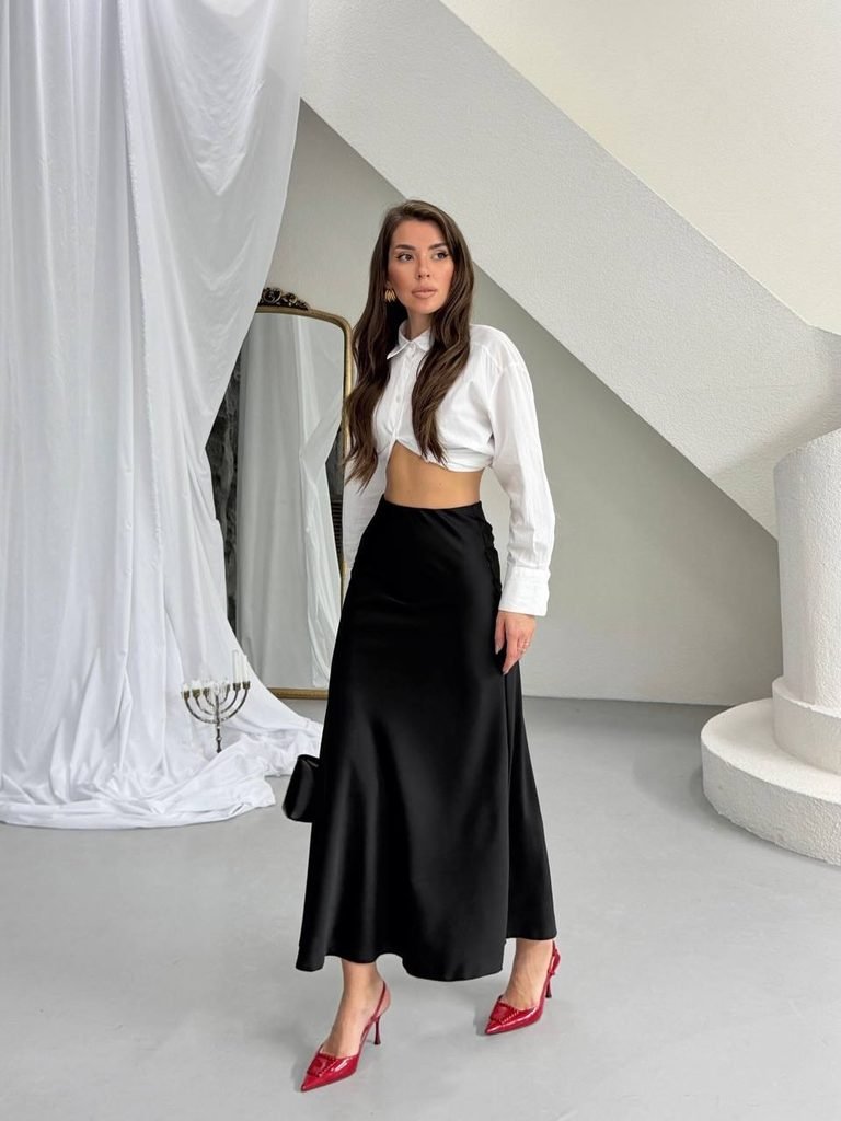 woman in a white crop shirt and black satin skirt with red heels