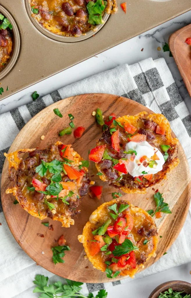 cheesy beef chili cups garnished with sour cream, tomatoes, and parsley on a platter