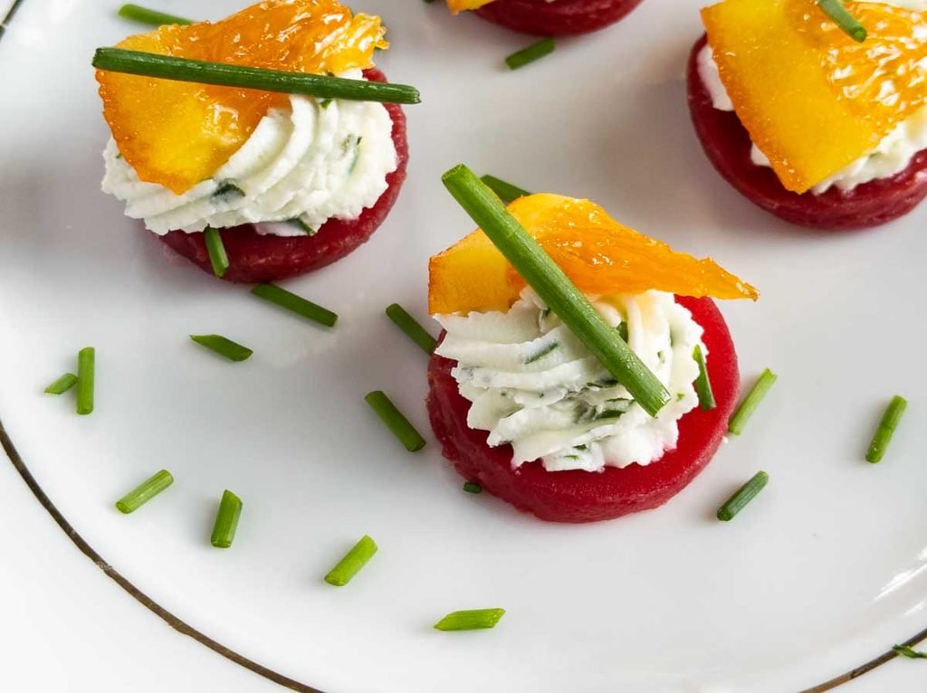 beet and goat cheese bites topped with citrus segments and chives on a plate