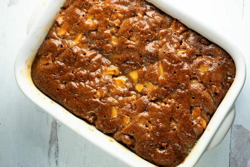 baked sticky caramel apple cake in a white ceramic baking dish