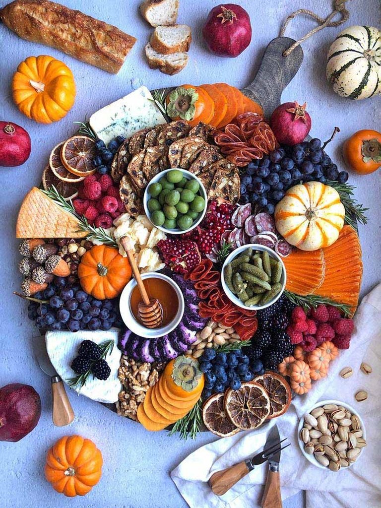 colorful fall appetizer charcuterie board filled with cheese, crackers, fruits, and small pumpkins