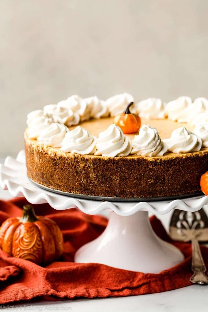 pumpkin cheesecake with whipped cream piping on a white cake stand