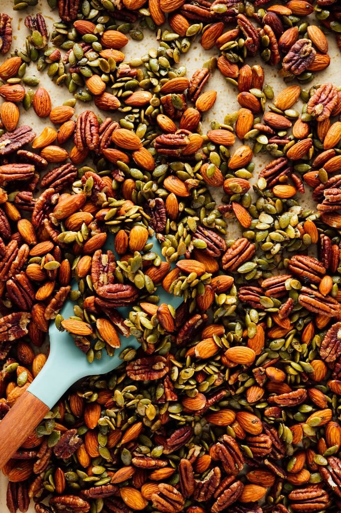 roasted party nuts mixture with pecans, almonds, and pumpkin seeds being stirred with a spatula