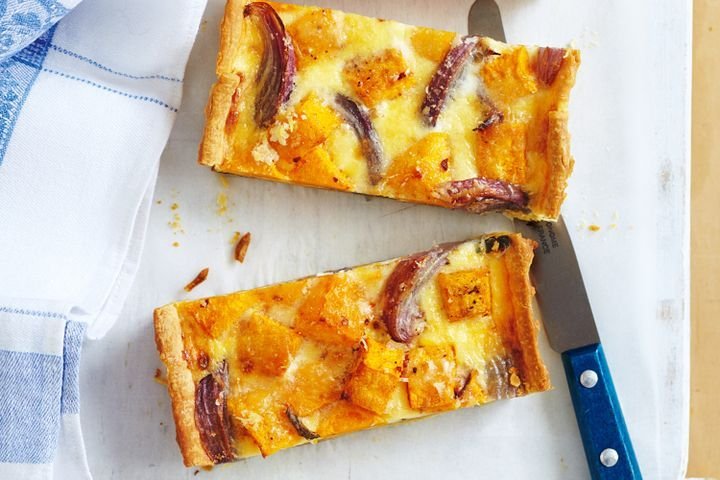 two rectangular slices of pumpkin sage tart on parchment paper next to a knife