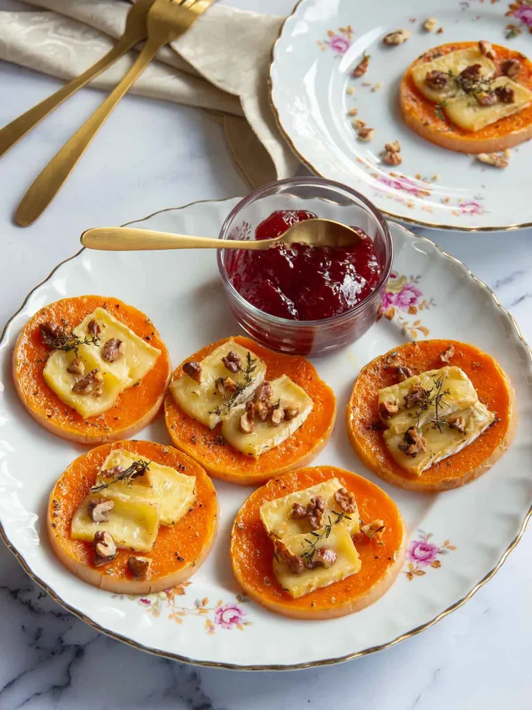 roasted butternut squash brie bites with melted cheese and walnuts next to cranberry sauce