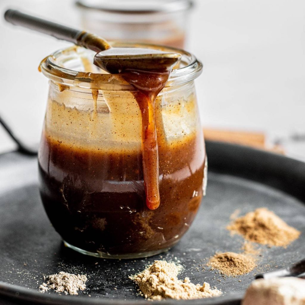 warm spiced caramel sauce dripping from a spoon into a glass jar