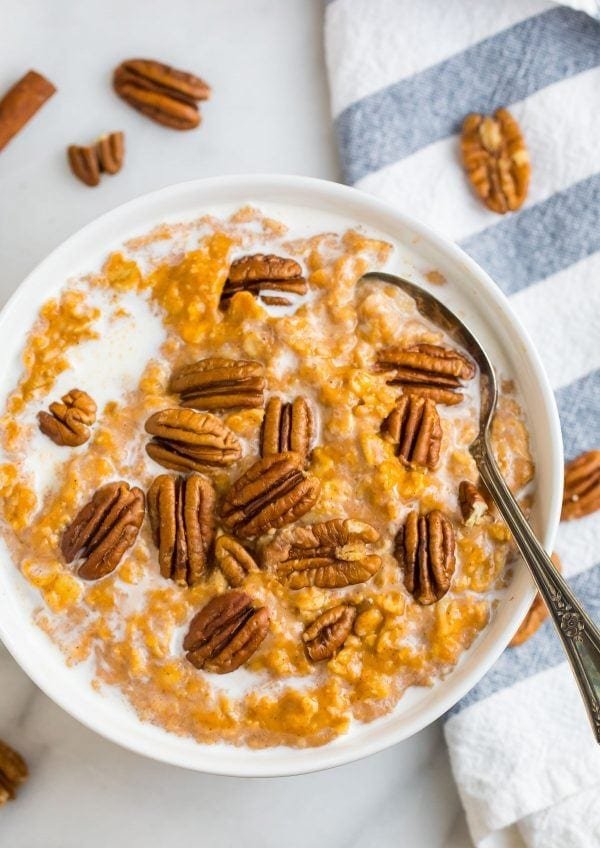 pumpkin oatmeal bowl topped with whole pecans and a drizzle of milk