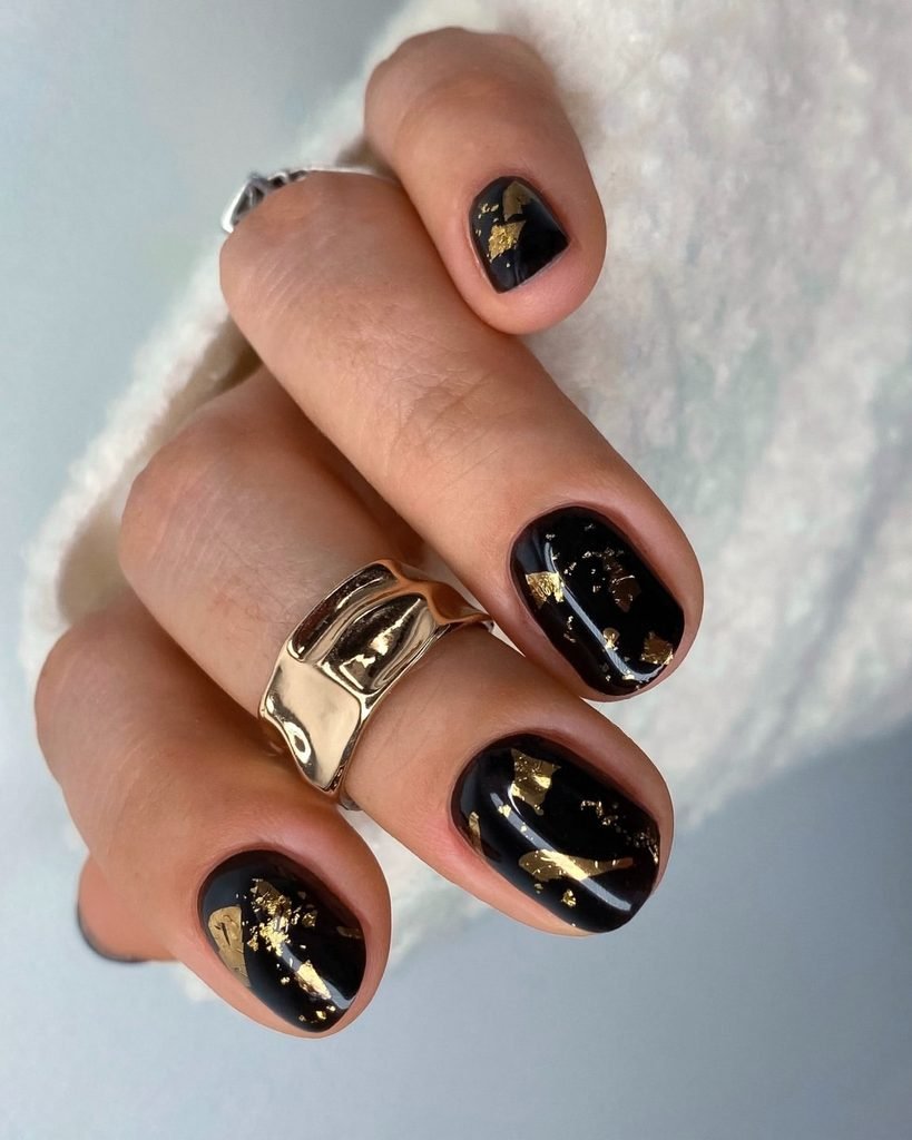 short round manicured nails painted black with metallic gold foil accents