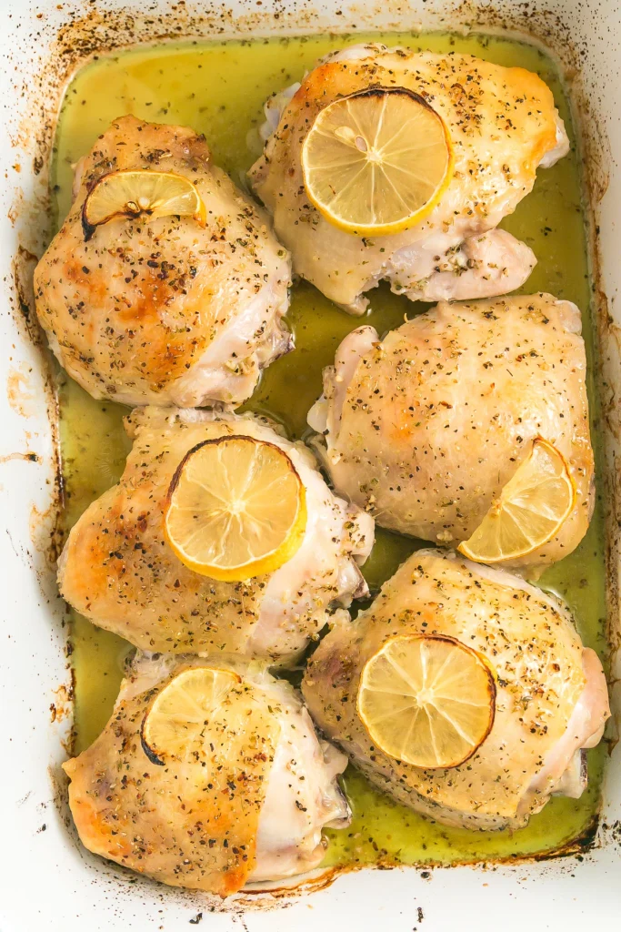 baked lemon herb chicken thighs topped with fresh lemon slices in a pan