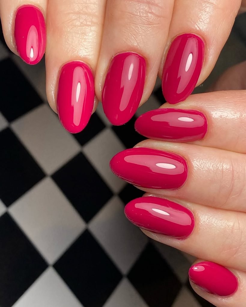 glossy bright magenta pink oval manicured nails against a checkered background