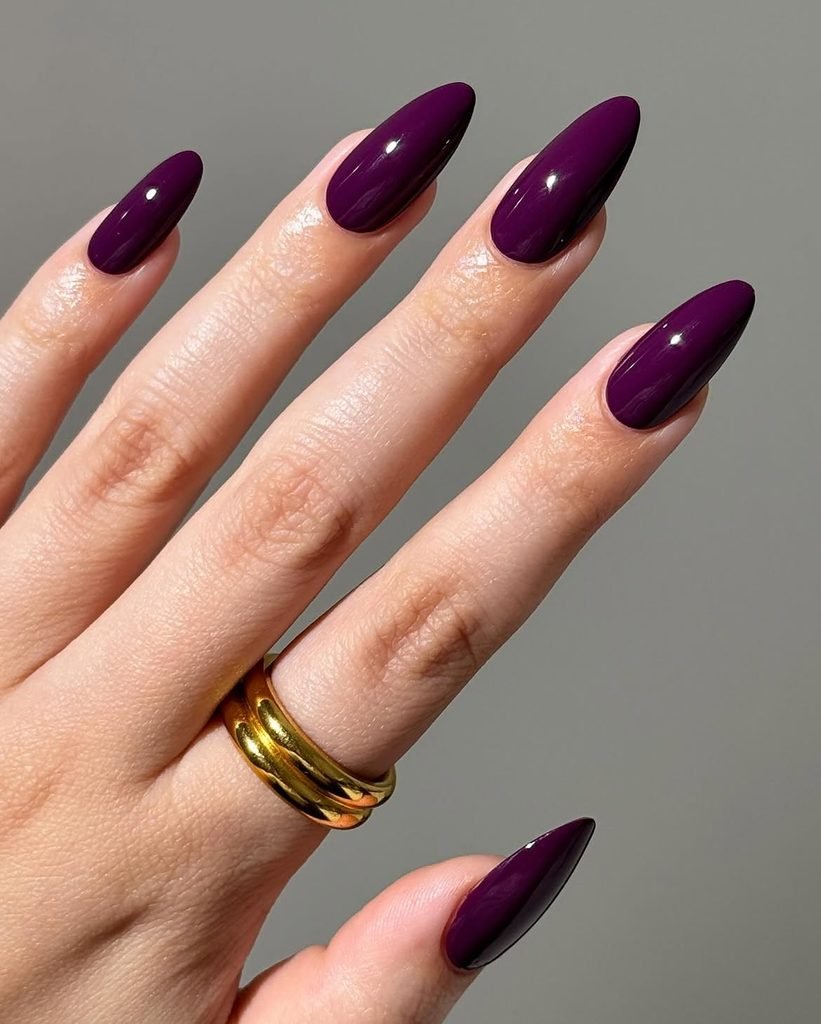 glossy deep plum purple almond nails on hand with gold rings