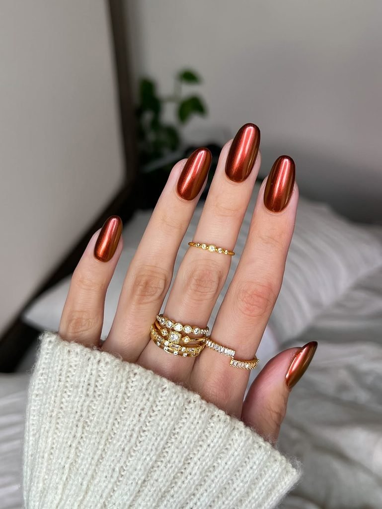 shiny bronze chrome oval nails styled with stacked gold rings