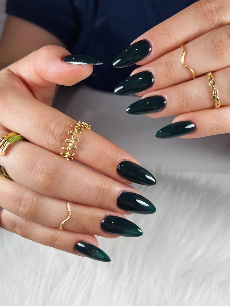 glossy dark emerald green almond-shaped nails worn with gold rings