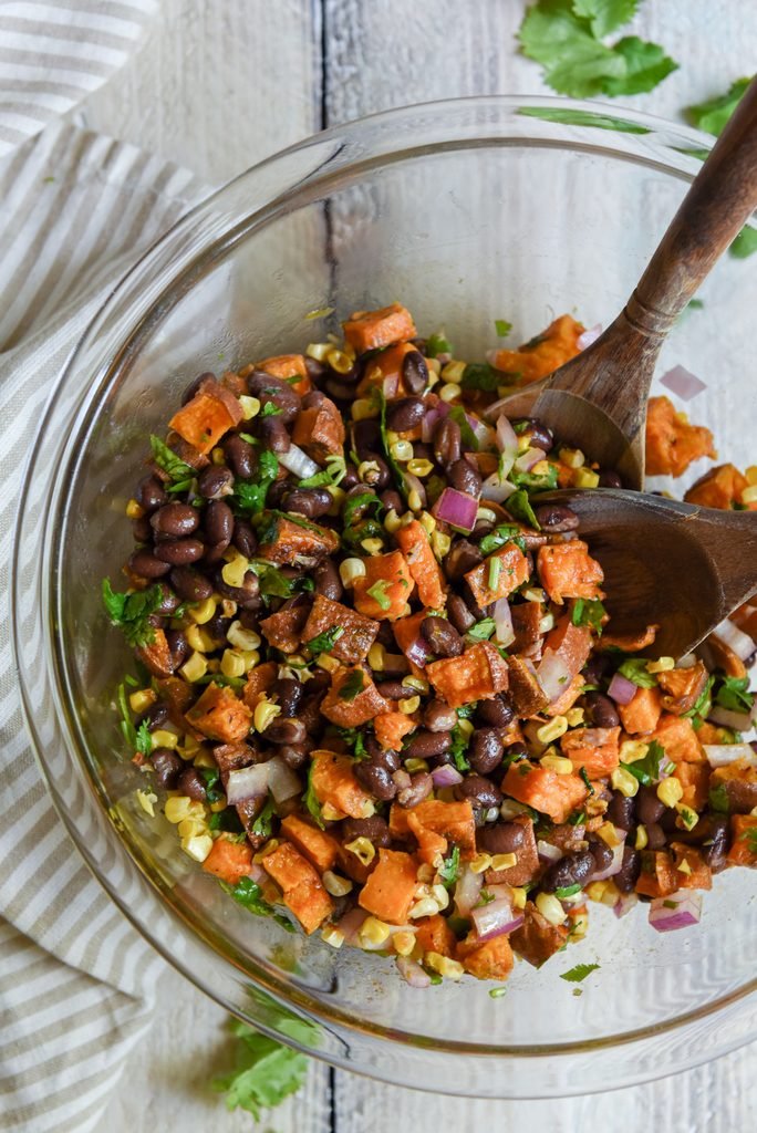 sweet potato and black bean salad with corn, red onion, and cilantro in a glass bowl