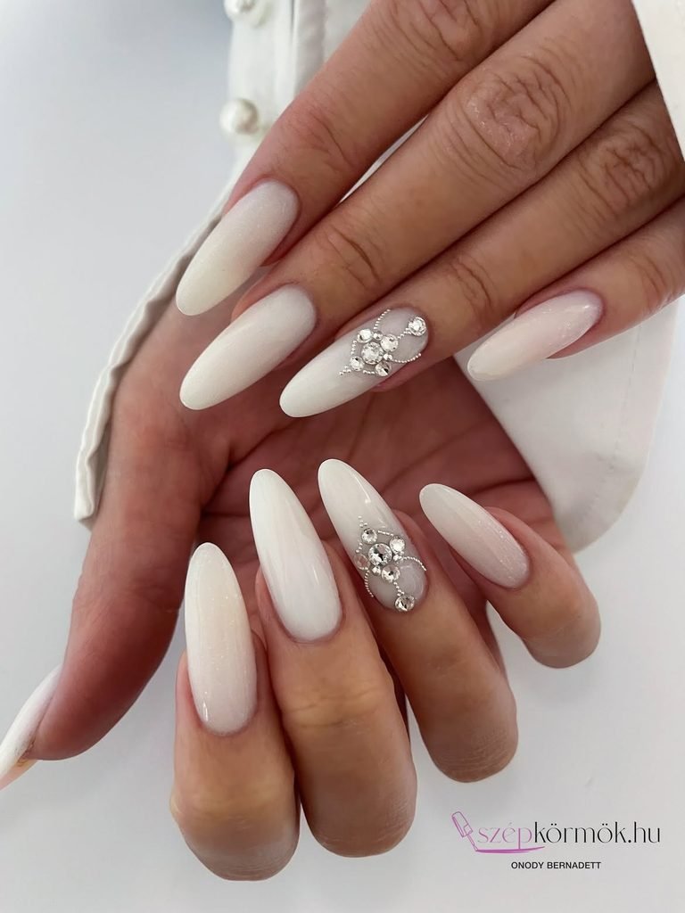 long almond milky white nails adorned with intricate jeweled rhinestone cluster nail art