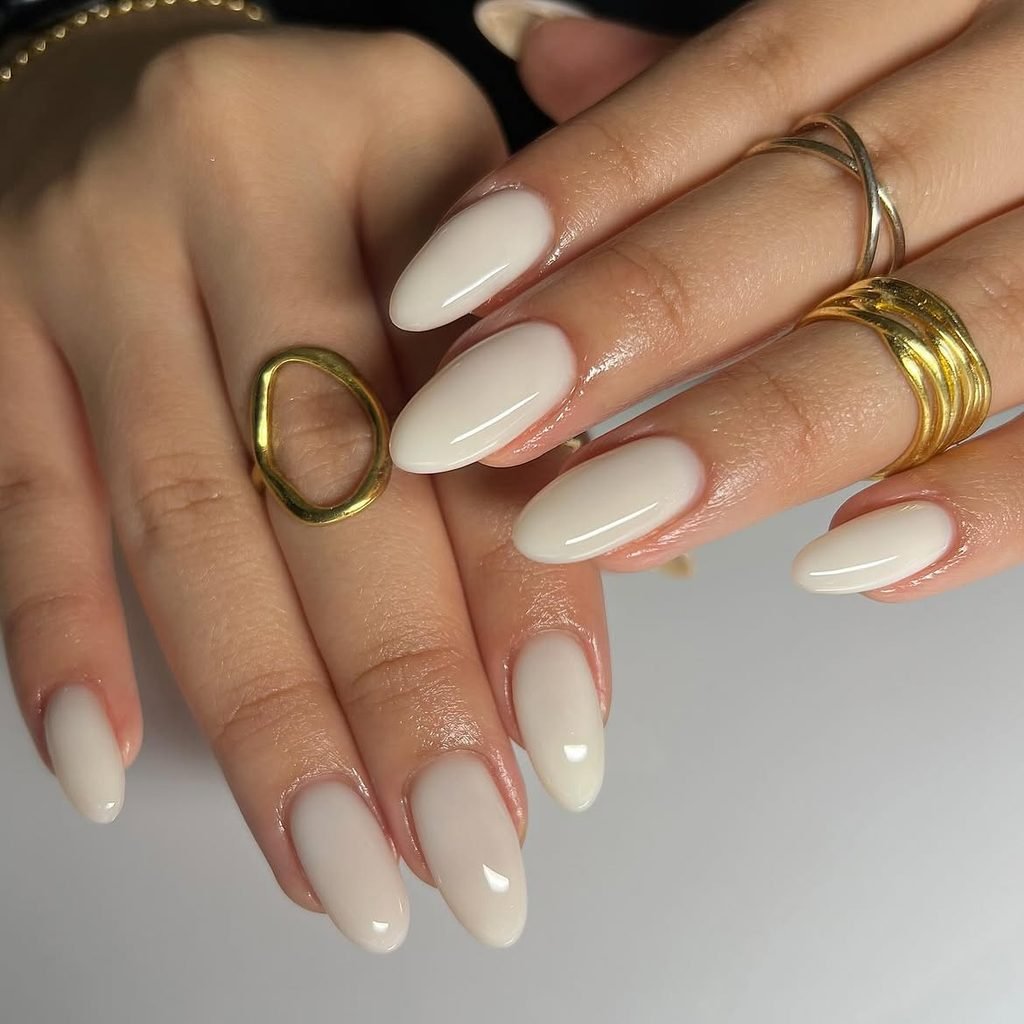 glossy milky white almond nails displayed on hands wearing gold rings