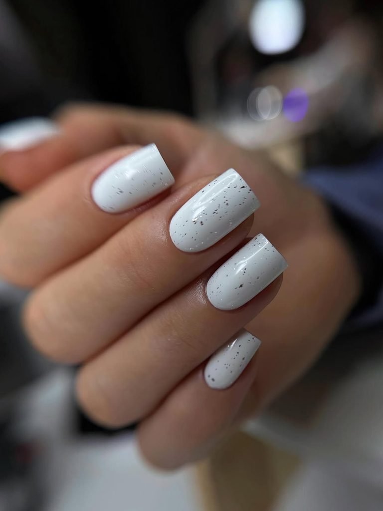 short square white nails with tiny dark flecks and a glossy gel finish