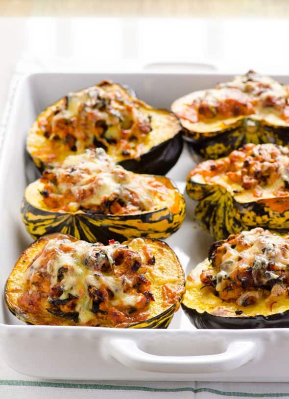 turkey stuffed acorn squash halves topped with melted cheese in a white baking dish