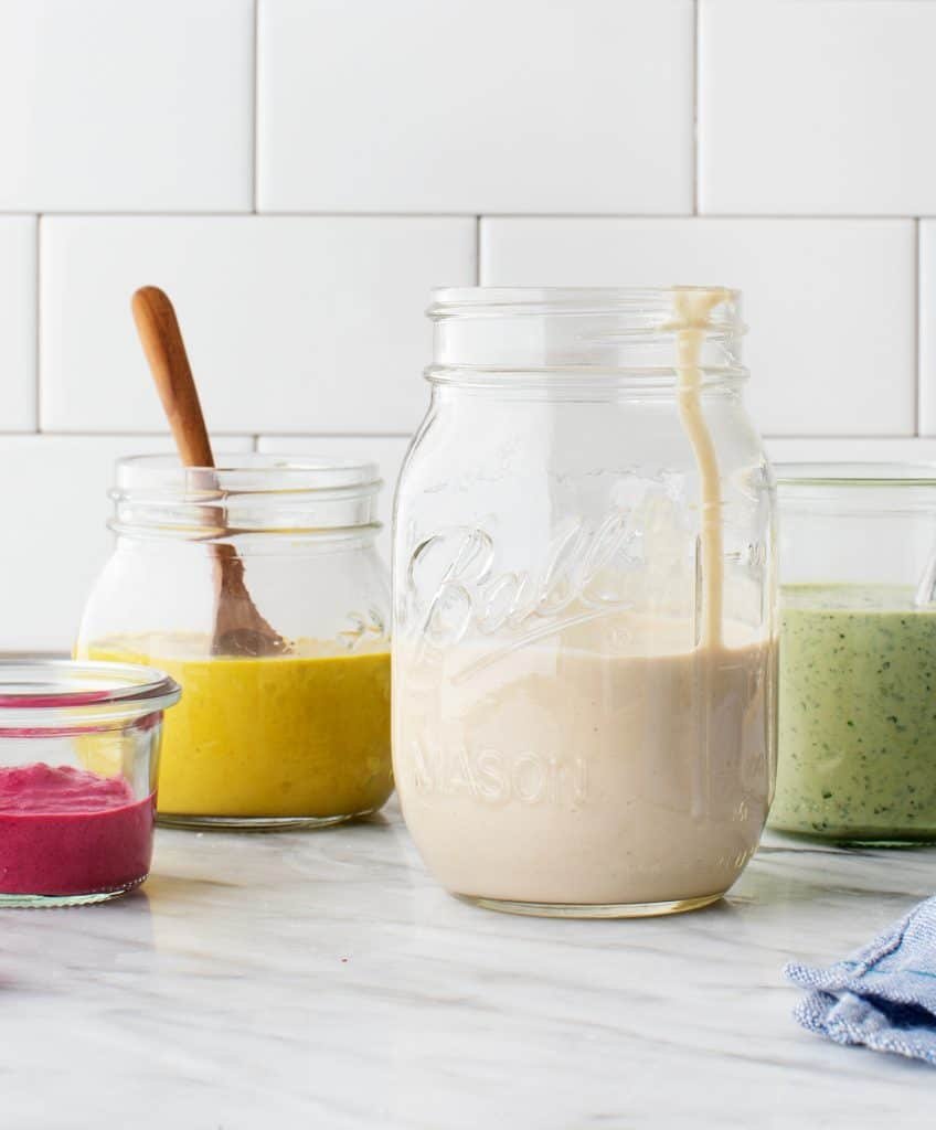 creamy tahini sauce in a mason jar alongside colorful homemade dressings