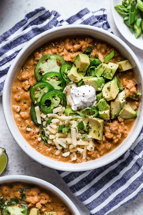 white bean chili topped with diced avocado, jalapeños, cheese, and sour cream