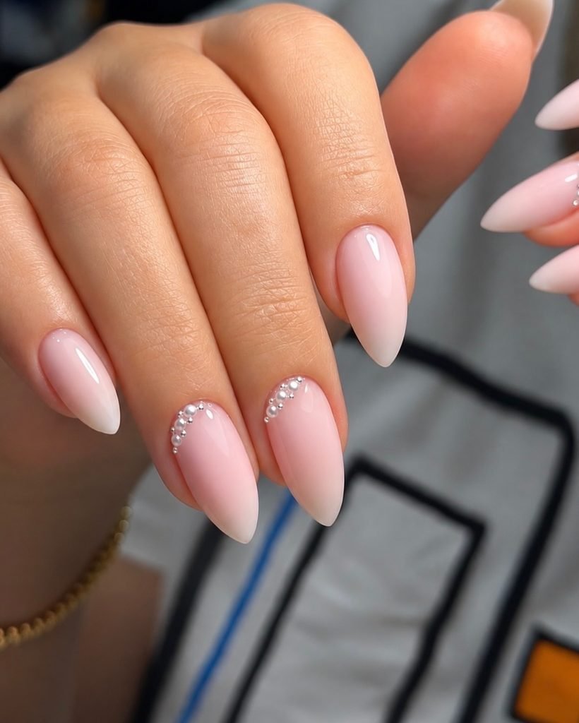 light pink almond nails with delicate pearl accents near the cuticle line