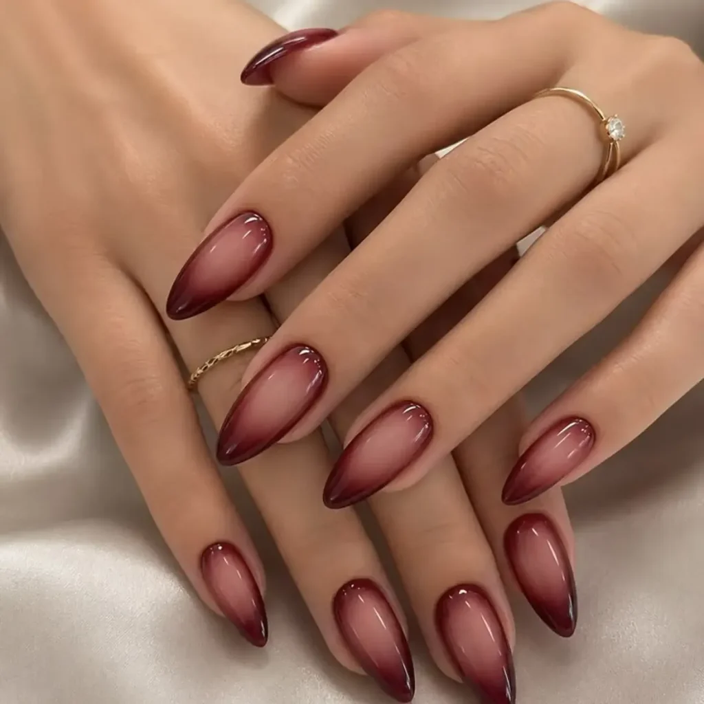 glossy dark red aura ombre almond nails on folded hands with gold rings