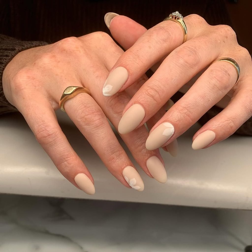 matte nude beige almond nails with subtle white floral accents