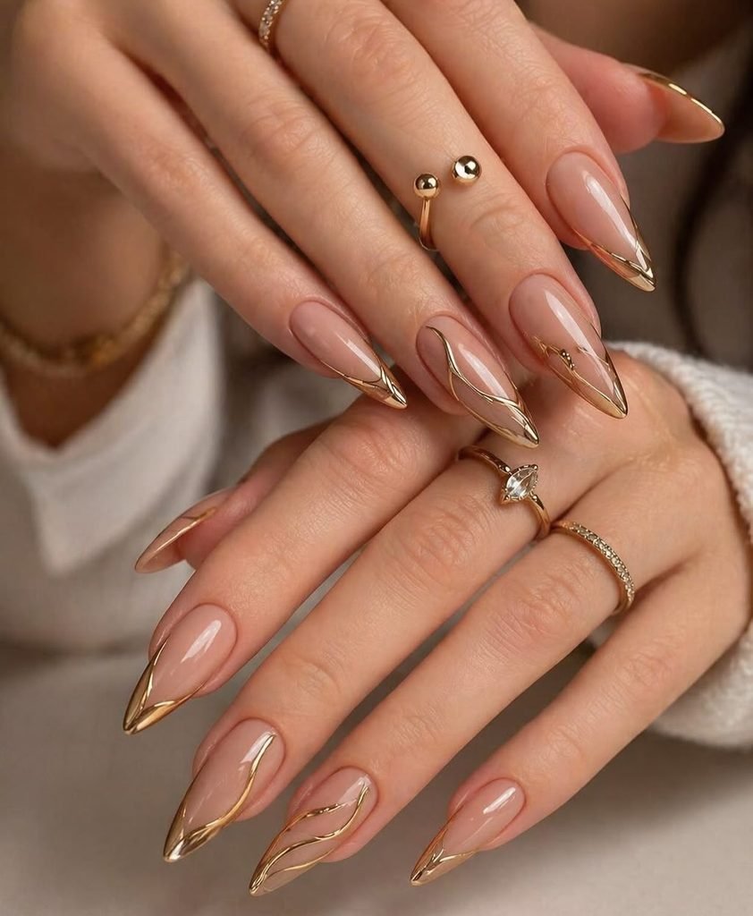 long nude almond nails decorated with intricate metallic gold line art