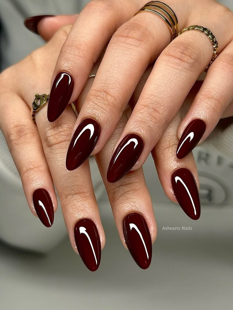 rich glossy dark maroon wine colored almond nails with thin gold rings