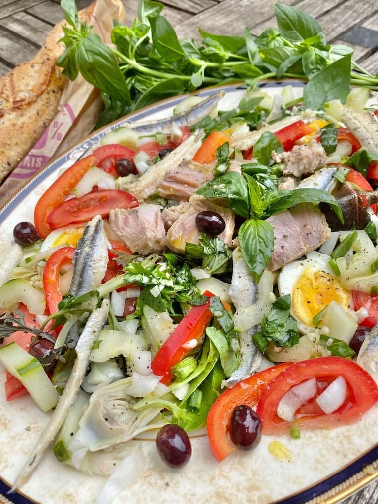 french nicoise salad topped with tuna, anchovies, hard-boiled eggs, and sliced tomatoes
