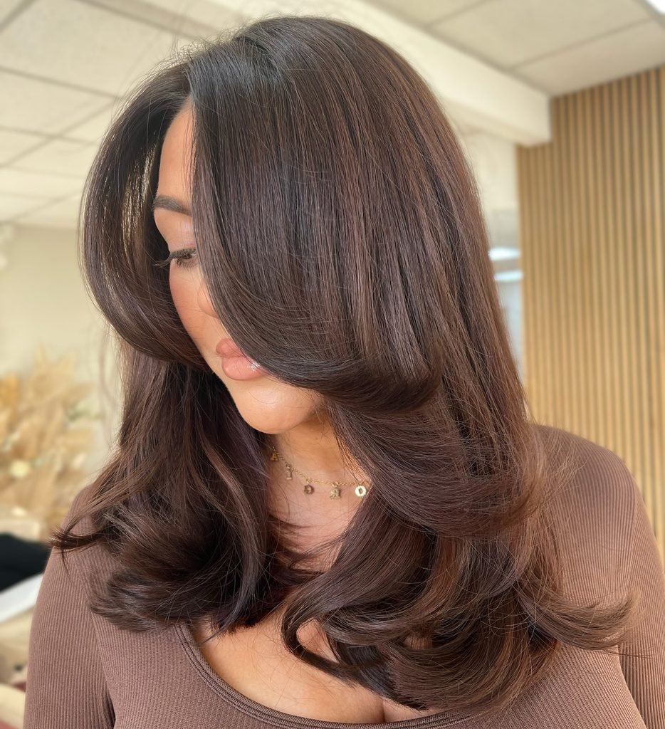layered brunette haircut with voluminous curtain bangs and softly curled ends