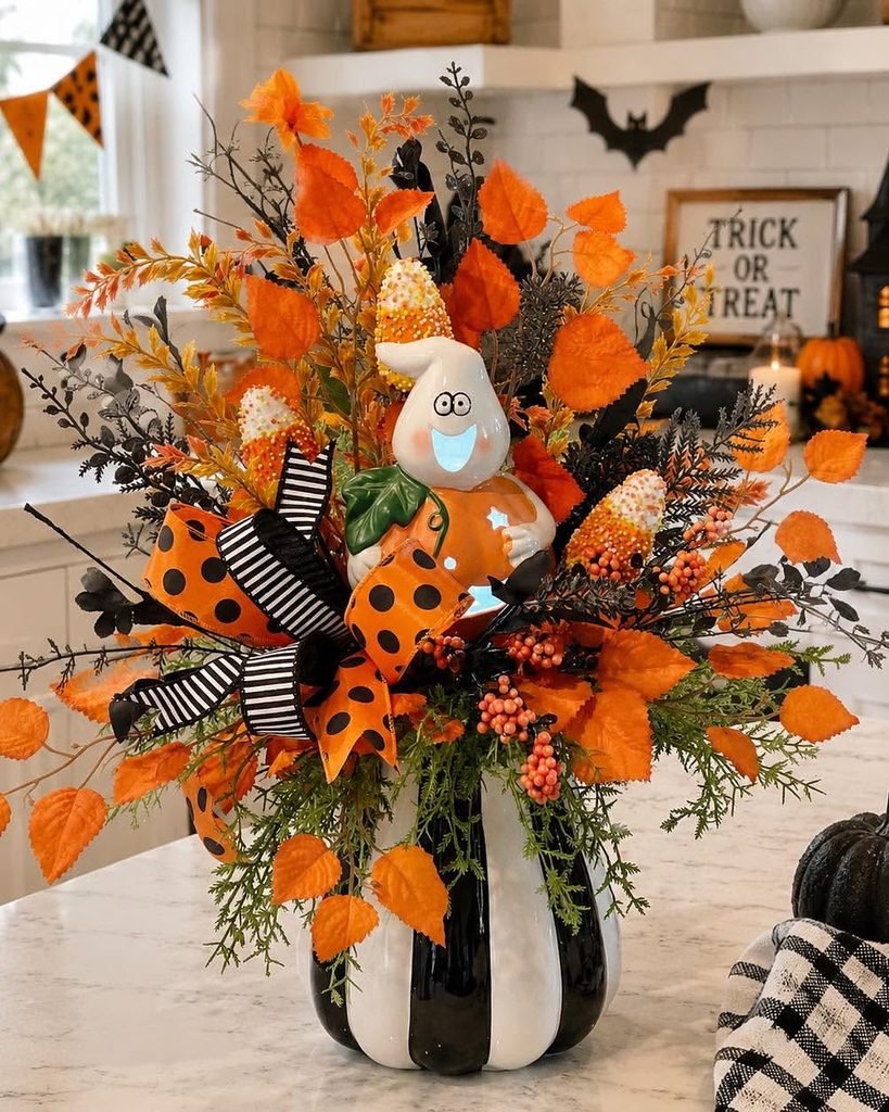 halloween floral centerpiece with orange autumn leaves, a ghost figurine, and striped ribbons